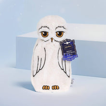 Load image into Gallery viewer, Harry Potter Hedwig hot water bottle cover by Mad Beauty, shaped like a soft white owl with embroidered details and hang tag, standing on a light blue surface with a blue backdrop.