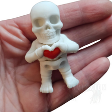 Load image into Gallery viewer, High-quality mini skeleton figure holding a red heart, featuring smooth articulation and a detailed design inside of hand for size comparison. Ideal as a desk companion, fidget, or collector’s display piece. By Convixxion.
