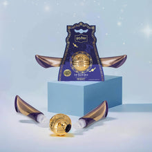 Load image into Gallery viewer, Harry Potter Golden Snitch lip balm duo by Mad Beauty, with the purple winged packaging displayed on a light blue block and the gold Snitch-shaped balm and two purple and gold squeeze tubes arranged in front on a soft blue background.
