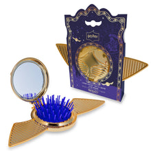 Load image into Gallery viewer, Harry Potter Golden Snitch pop-up brush and mirror set by Mad Beauty, shown with the gold winged compact open to reveal a round mirror and blue bristle hair brush beside the purple Golden Snitch-themed packaging on a white background.
