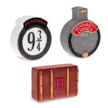 Load image into Gallery viewer, Angled view of three Harry Potter bath fizzers by Mad Beauty shaped like the Platform 9 3/4 sign, the Hogwarts Express engine front, and a brown Hogwarts luggage trunk with an “H,” all standing on a white surface.

